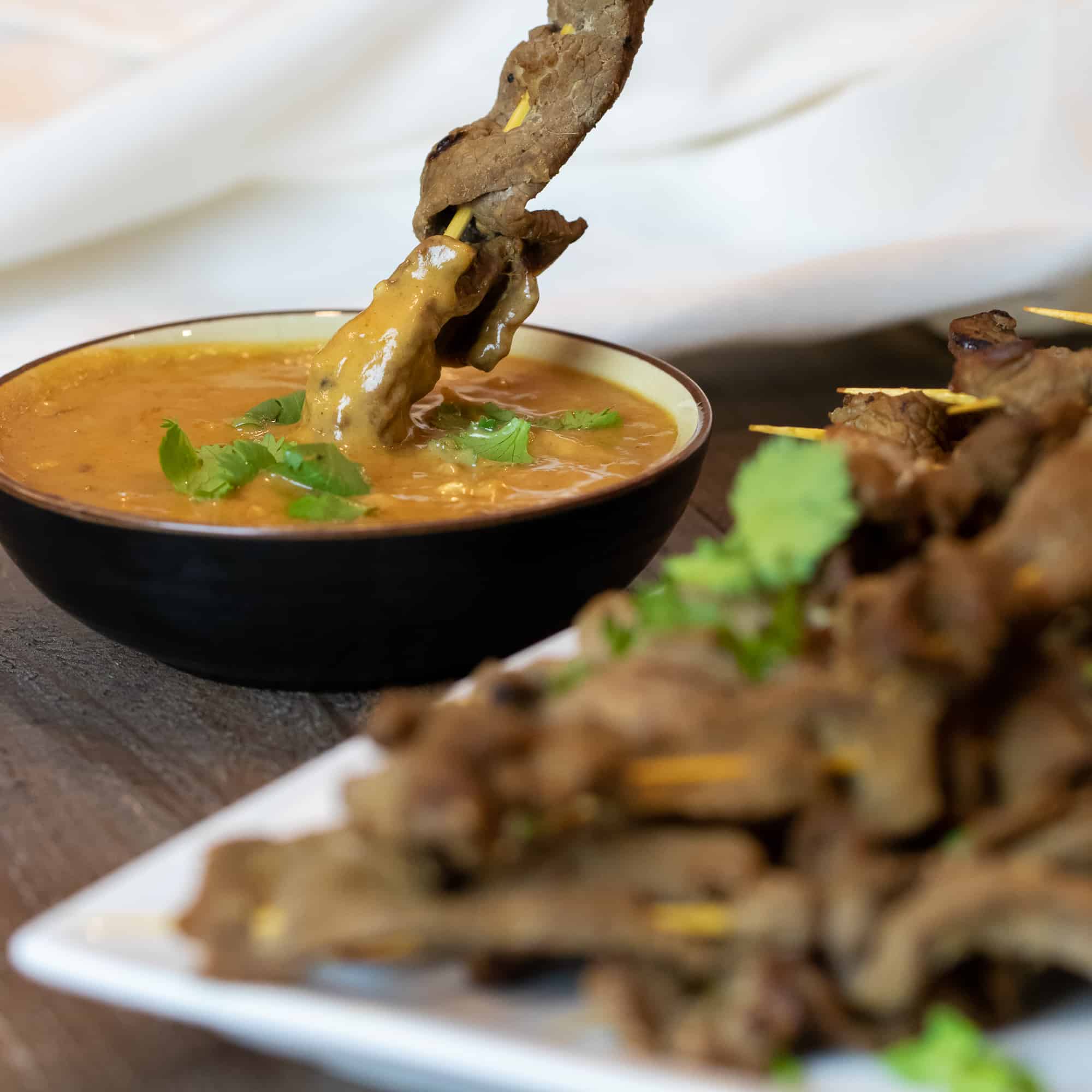 Dipping a beef satay skewer in a bowl of Thai peanut sauce.