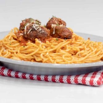 A plate of spaghetti topped with four meatballs and sauce.