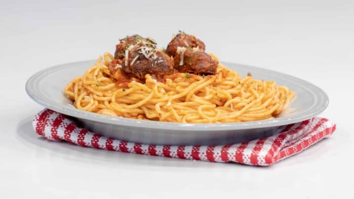 A plate of spaghetti topped with four meatballs and sauce.