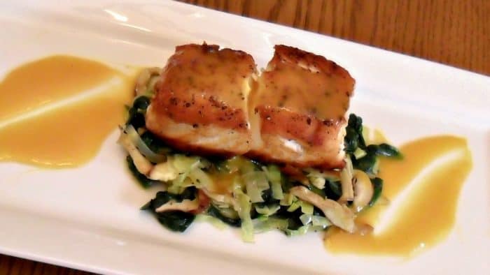 A pan seared filet of halibut served on a bed of sauteed leeks, spinach and oyster mushrooms drizzled with a honey mustard sauce.