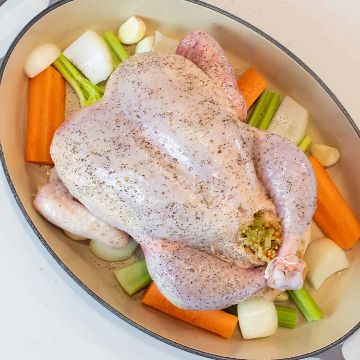 Stuffing chicken in a roasting dish with a bed of vegetables.