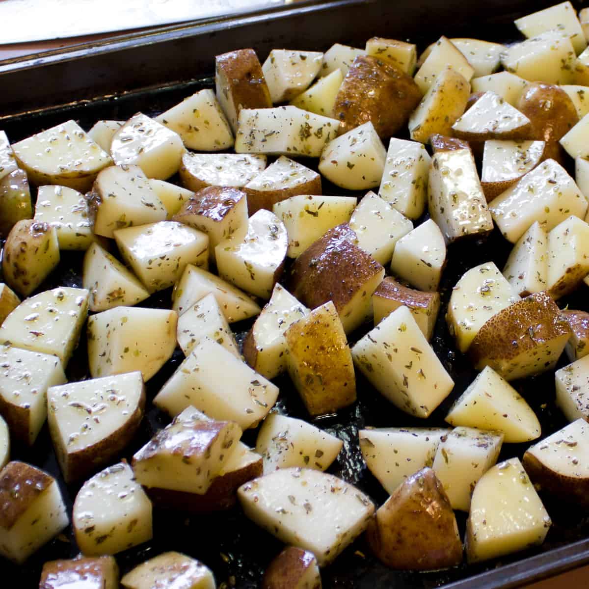 Diced raw potatoes tossed with seasoning and on a baking sheet ready to go in the oven.