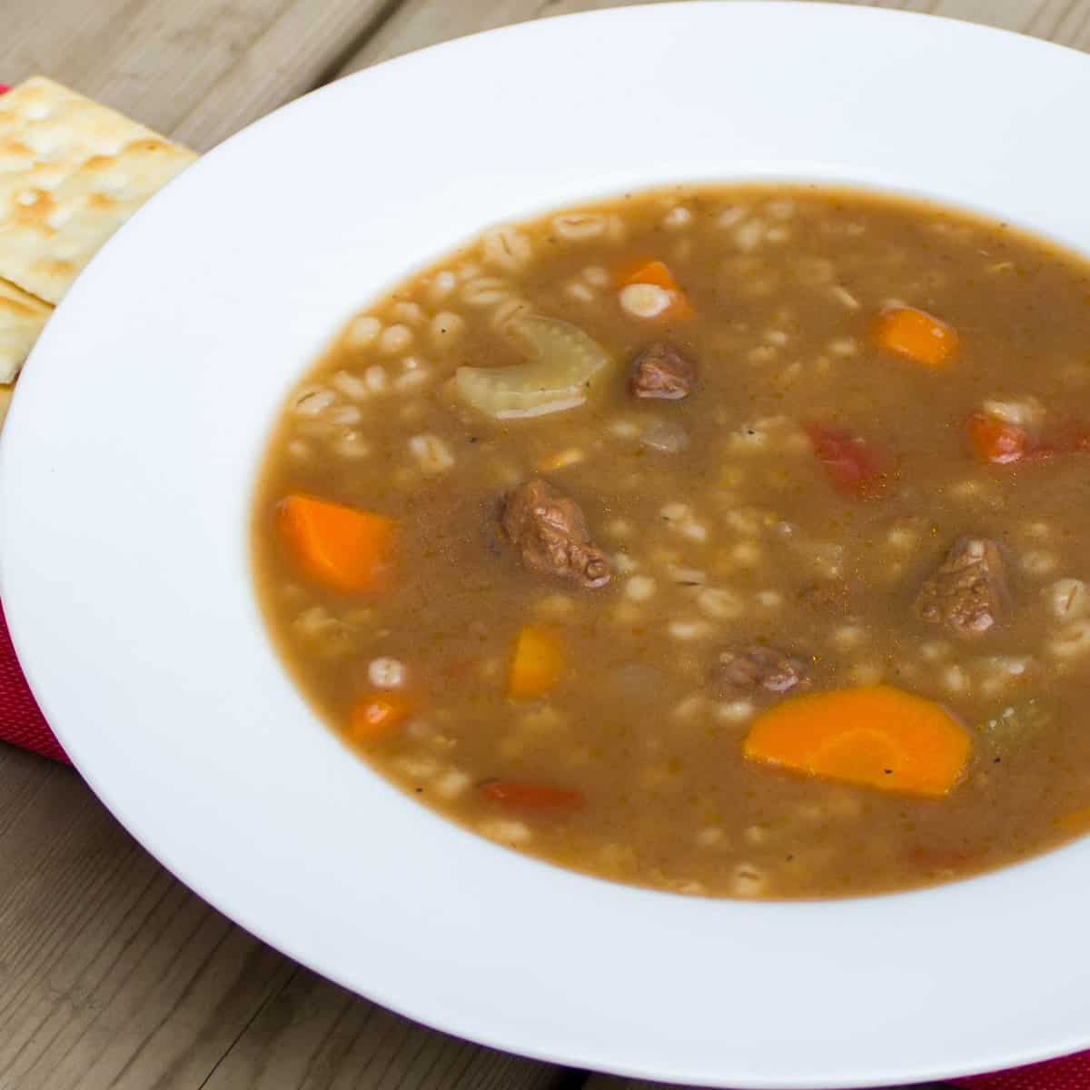 A bowl of soup with some saltine crackers for crumbling.  Beef Barley Soup Beef Barley Soup square 2