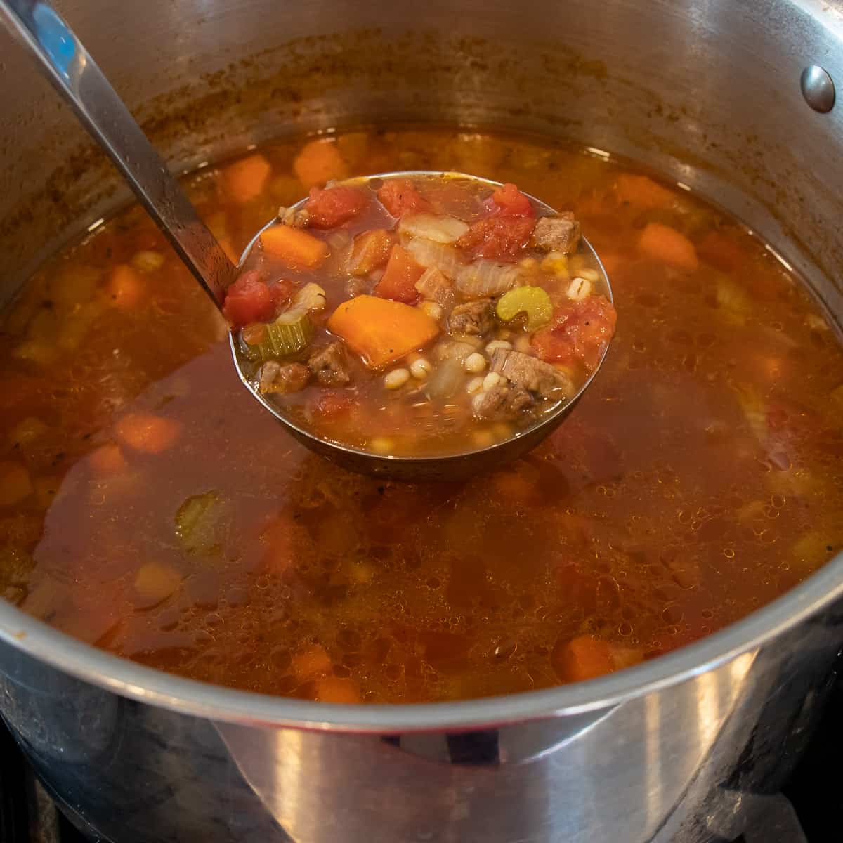 Scooping a ladle of fresh soup out of a large stock pot