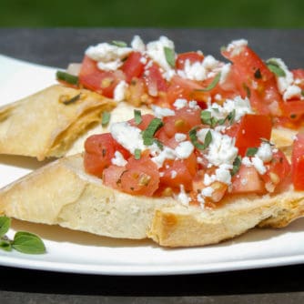 Recipe for how to make bruschetta bread with roma tomatoes, garlic, onion, lemon juice and olive oil. Topped with feta and oregano on a toasted slice of French baguette.