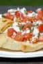 Recipe for how to make bruschetta bread with roma tomatoes, garlic, onion, lemon juice and olive oil. Topped with feta and oregano on a toasted slice of French baguette.