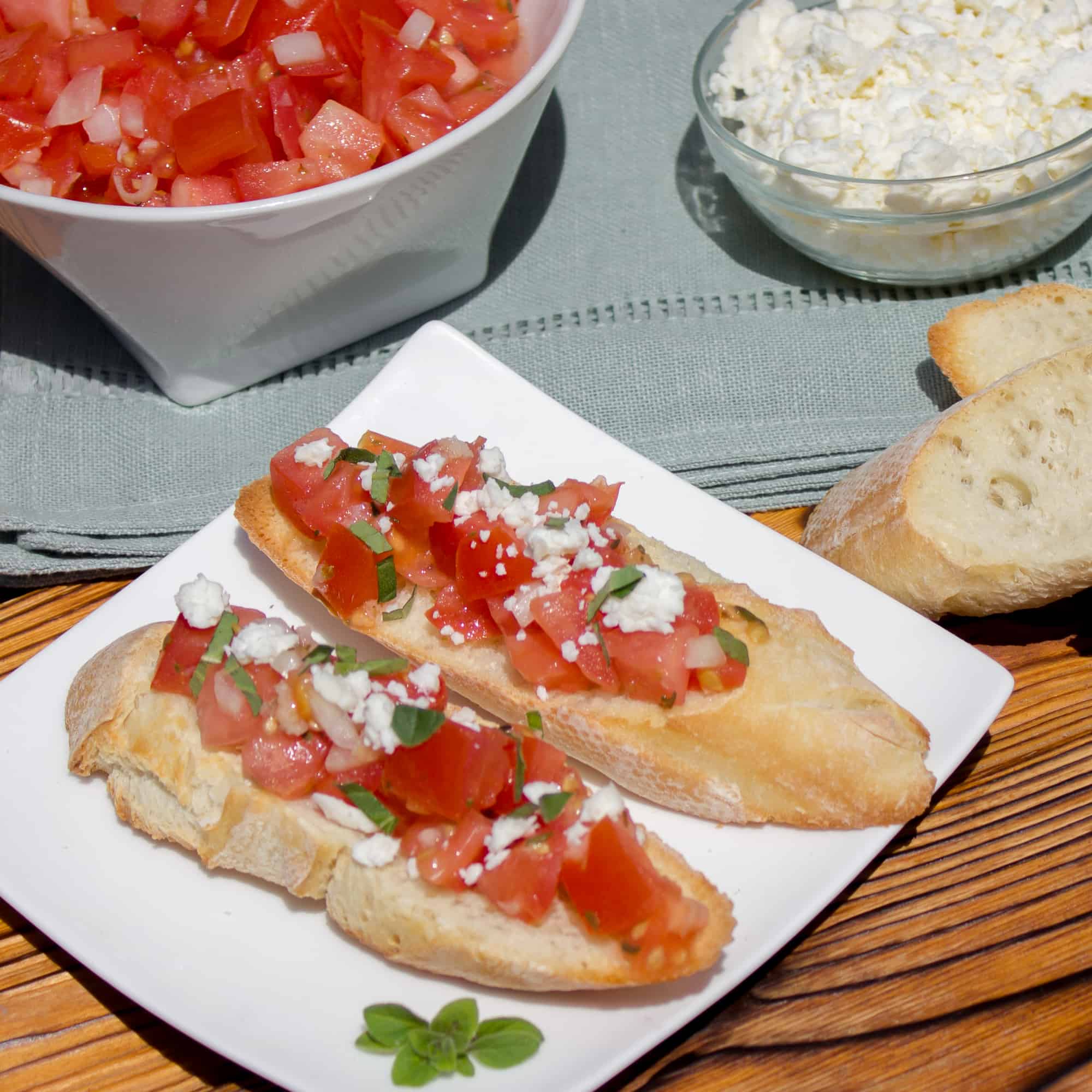 Recipe for how to make bruschetta bread with roma tomatoes, garlic, onion, lemon juice and olive oil. Topped with feta and oregano on a toasted slice of French baguette. 