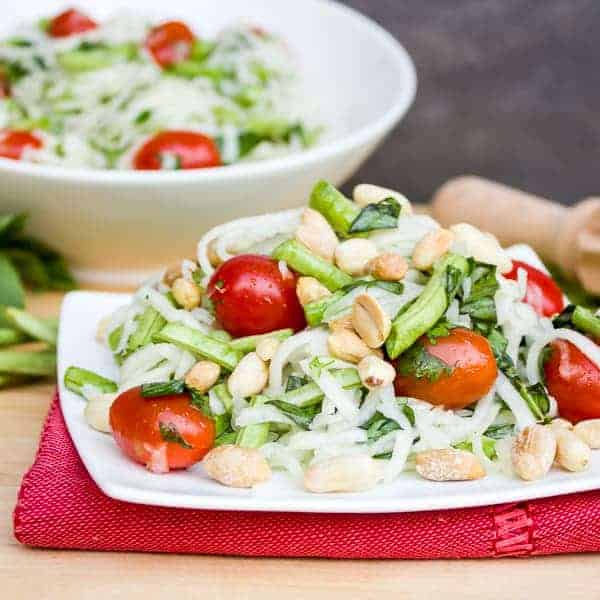 Thai green papaya salad recipe with grape tomatoes, peanuts, long green beans, thai basil, cilantro and a dressing made of lime juice, oil, fish sauce, sugar, thai chilies.