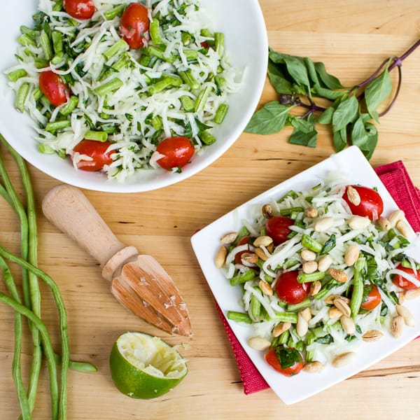 Thai green papaya salad recipe with grape tomatoes, peanuts, long green beans, thai basil, cilantro and a dressing made of lime juice, oil, fish sauce, sugar, thai chilies.