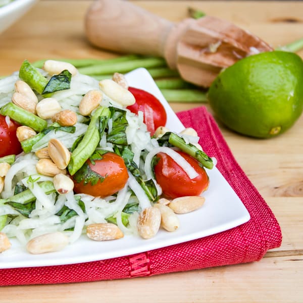 Thai green papaya salad recipe with grape tomatoes, peanuts, long green beans, thai basil, cilantro and a dressing made of lime juice, oil, fish sauce, sugar, thai chilies.