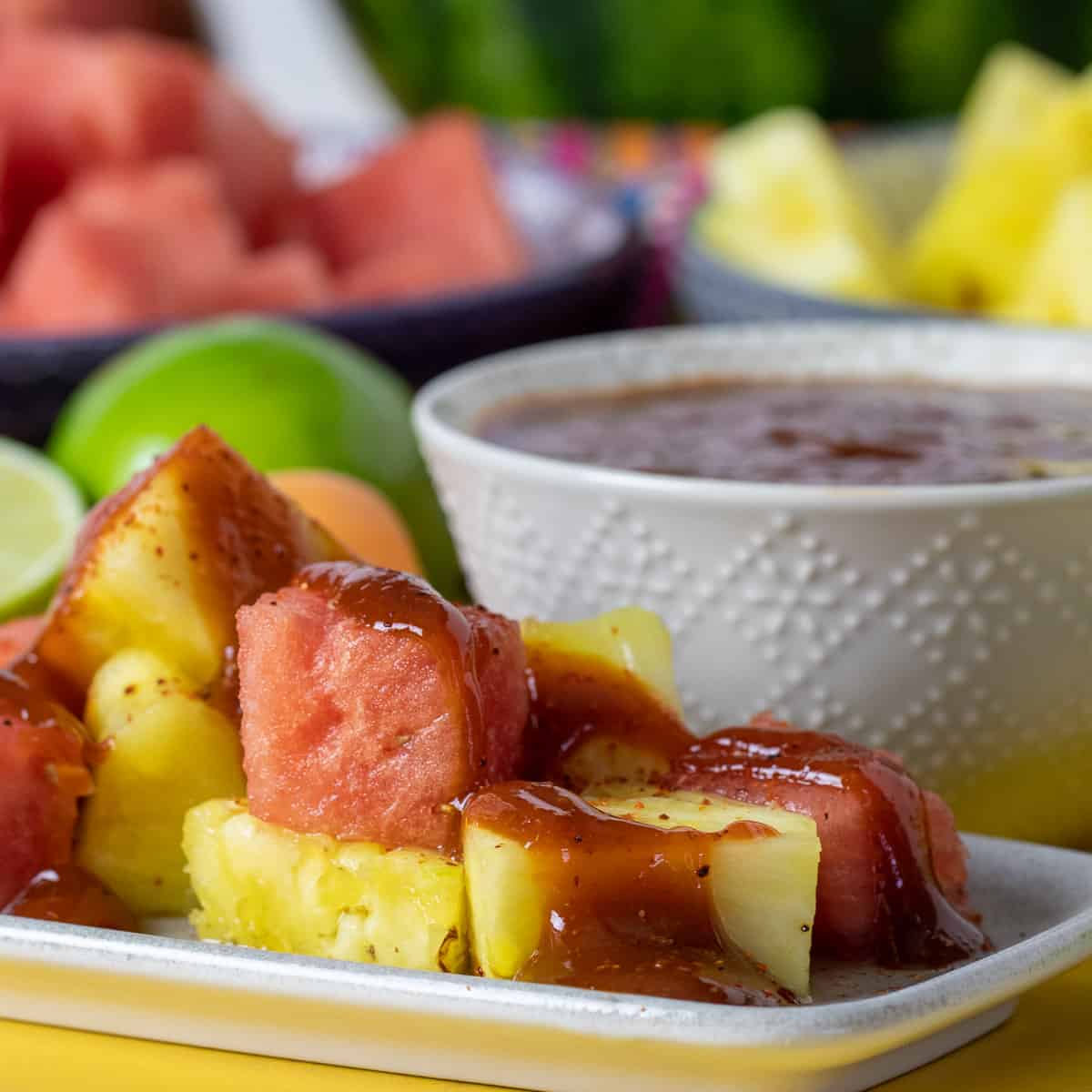 Close up picture of cut watermelon and pineapple with sauce poured all over them.