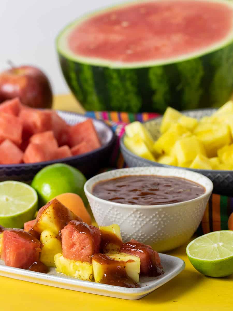 Plate of chopped watermelon and pineapple with bowl of chamoy sauce.