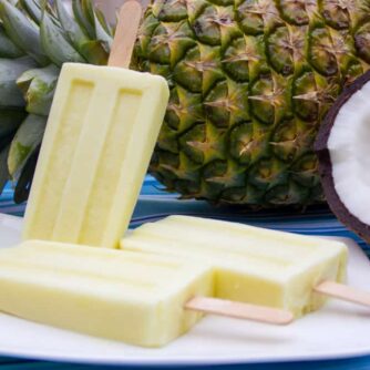 Popsicles on a plate with a pineapple and coconut behind the plate.