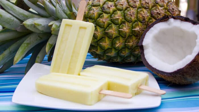 Popsicles on a plate with a pineapple and coconut behind the plate.