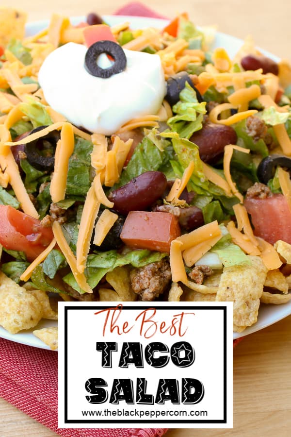 Taco salad recipe with romaine lettuce, ground beef, tomatoes, kidney beans, black olives, cheddar cheese, sour cream and Frito corn chips or nacho chips.