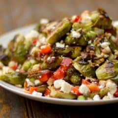 Roasted Brussels sprout salad recipe with bacon, walnuts, feta cheese, green onions, re peppers and a balsamic vinaigrette.