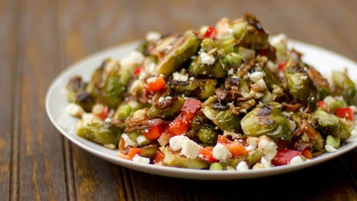 Roasted Brussels sprout salad recipe with bacon, walnuts, feta cheese, green onions, re peppers and a balsamic vinaigrette.