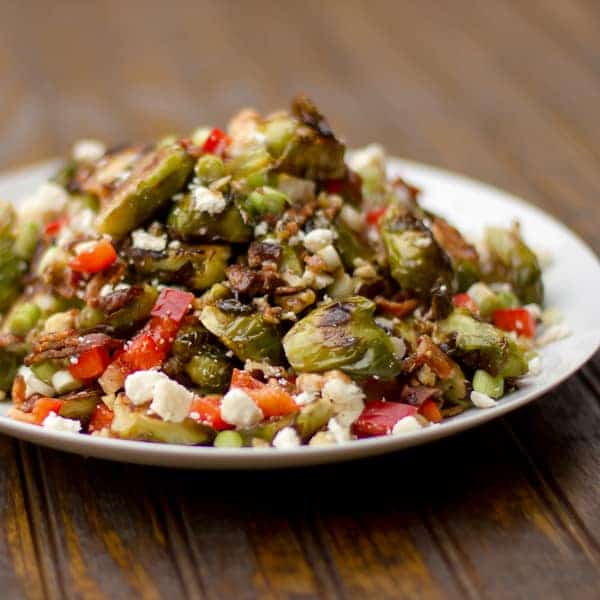 Roasted Brussels sprout salad recipe with bacon, walnuts, feta cheese, green onions, re peppers and a balsamic vinaigrette.