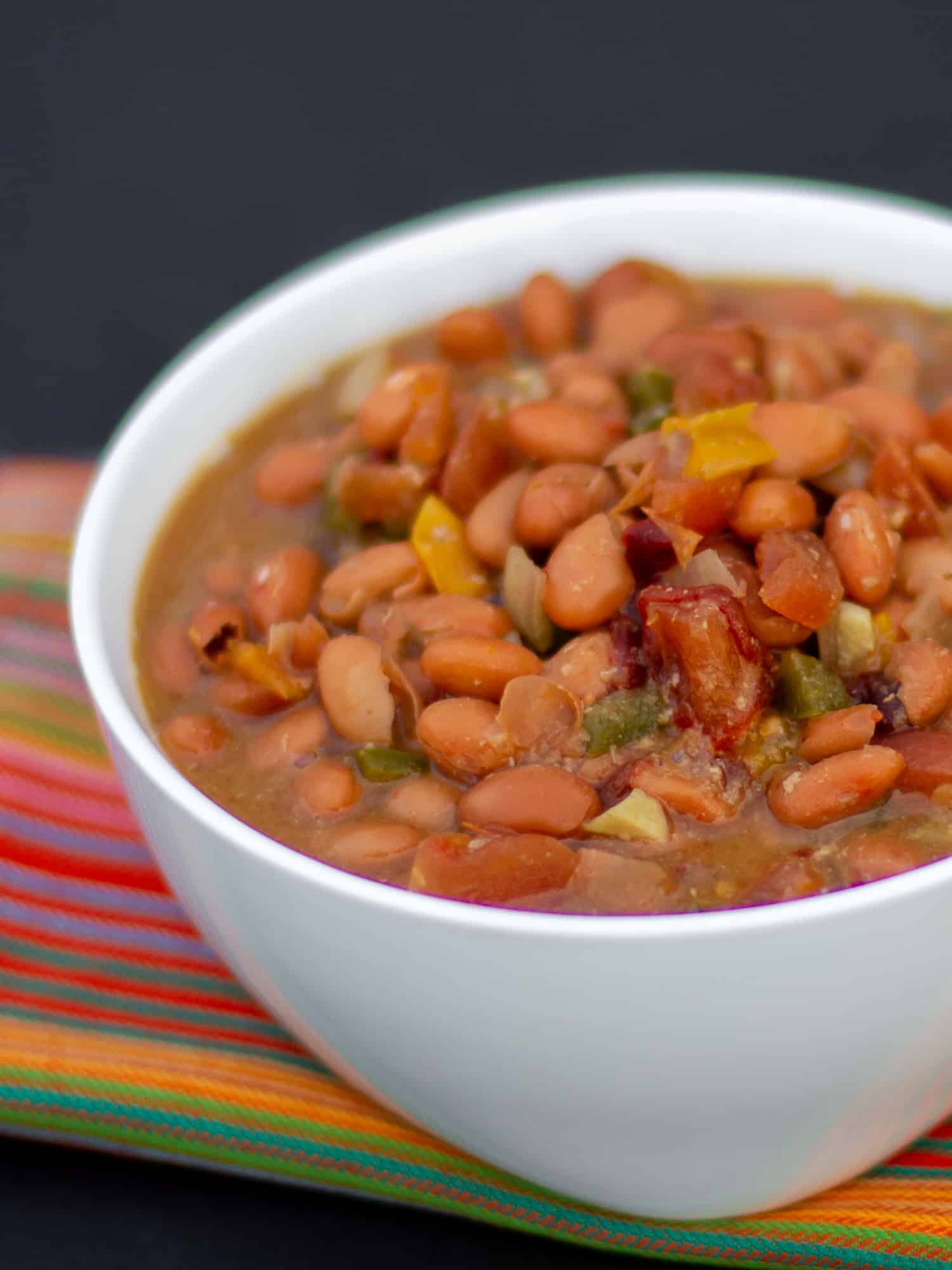 Slow cooked pinto beans with ham hock, tomato, onion, jalapeno and ancho chilies. Amazing tex-mex / Mexican comfort food baked bean recipe made in a Crock Pot.