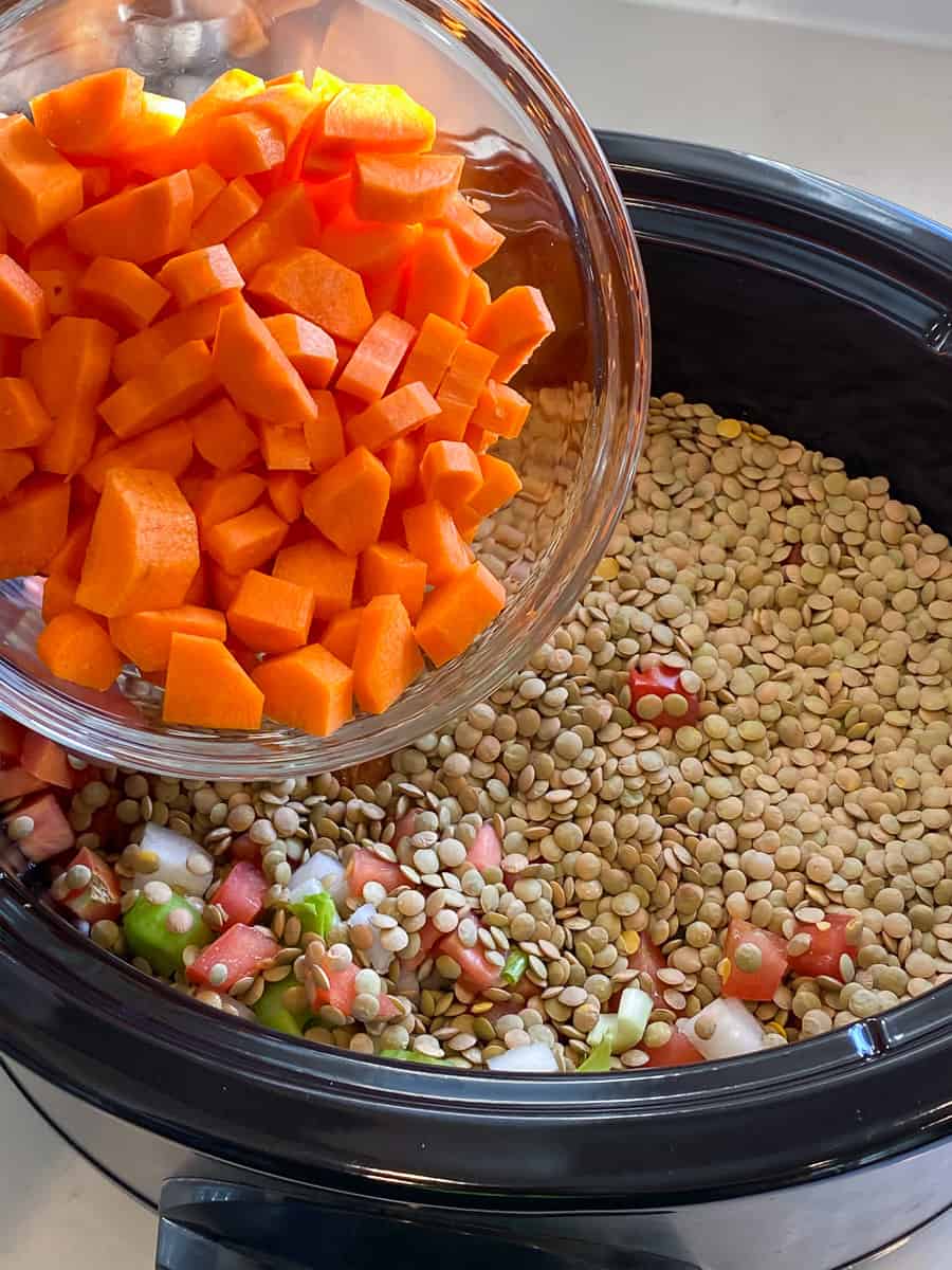 Dumping a bowl of chopped carrots into a slow cooker.