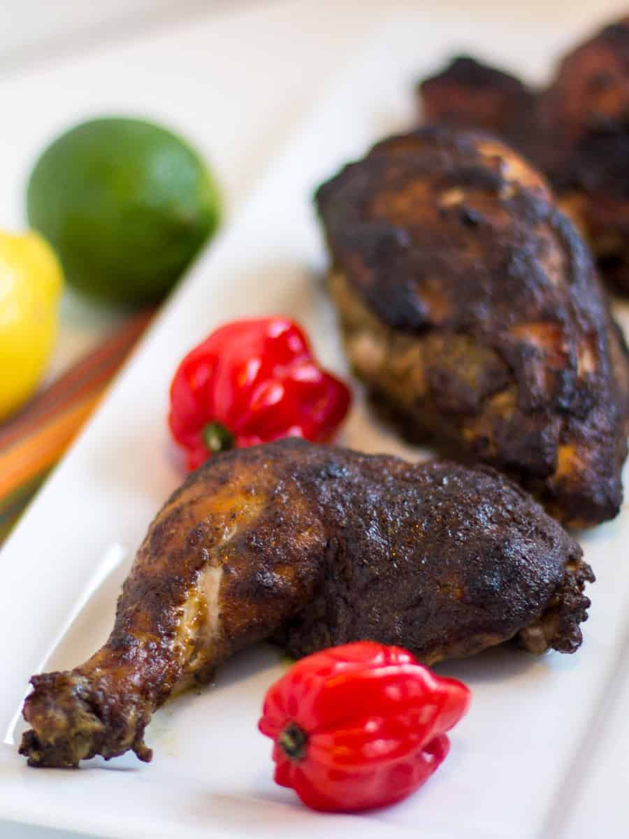 a tall image of a plate of jerk chicken with scotch bonnet peppers and lemon