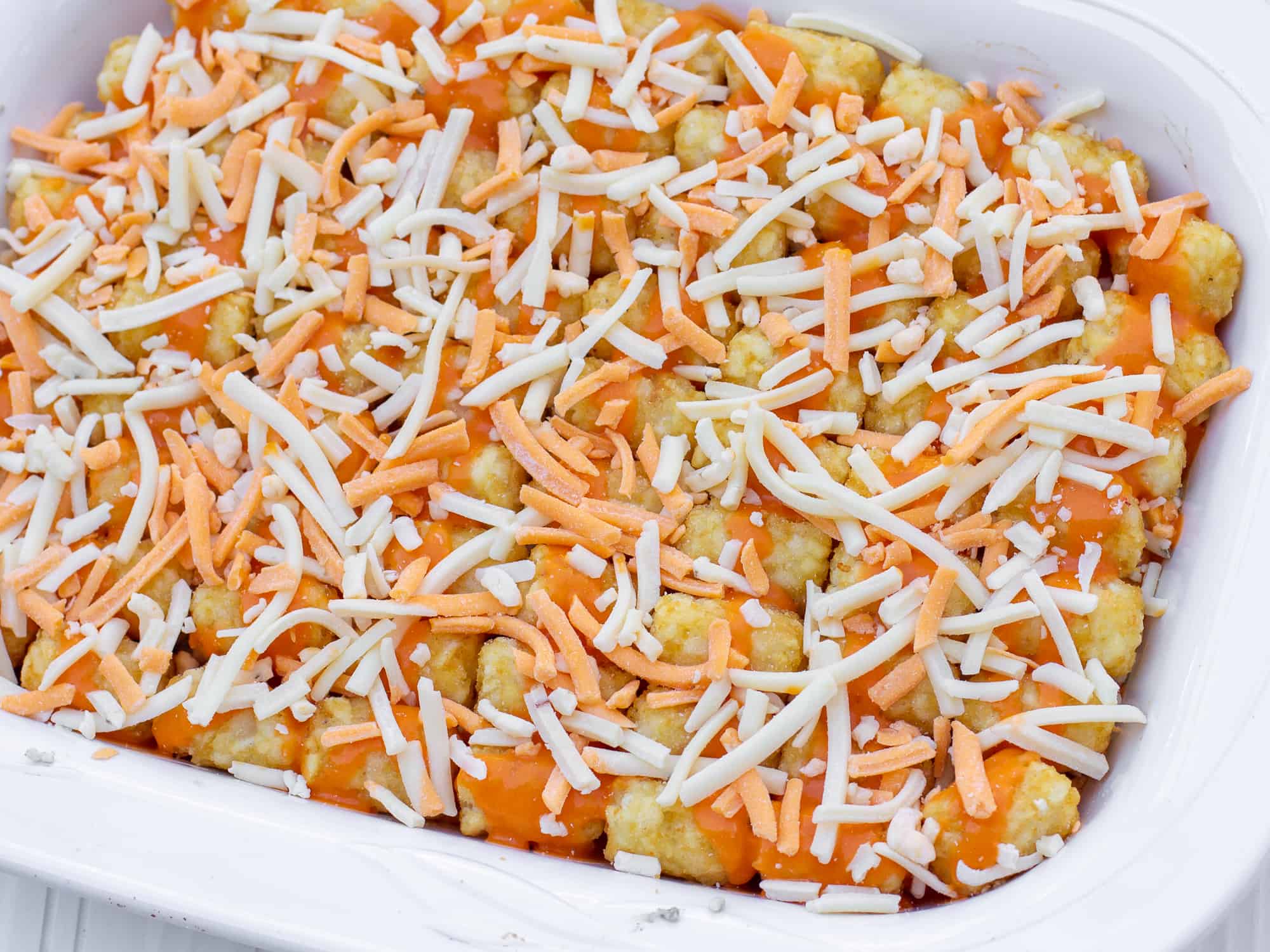 Place Tate Tots on top and drizzle with buffalo sauce and grated cheese