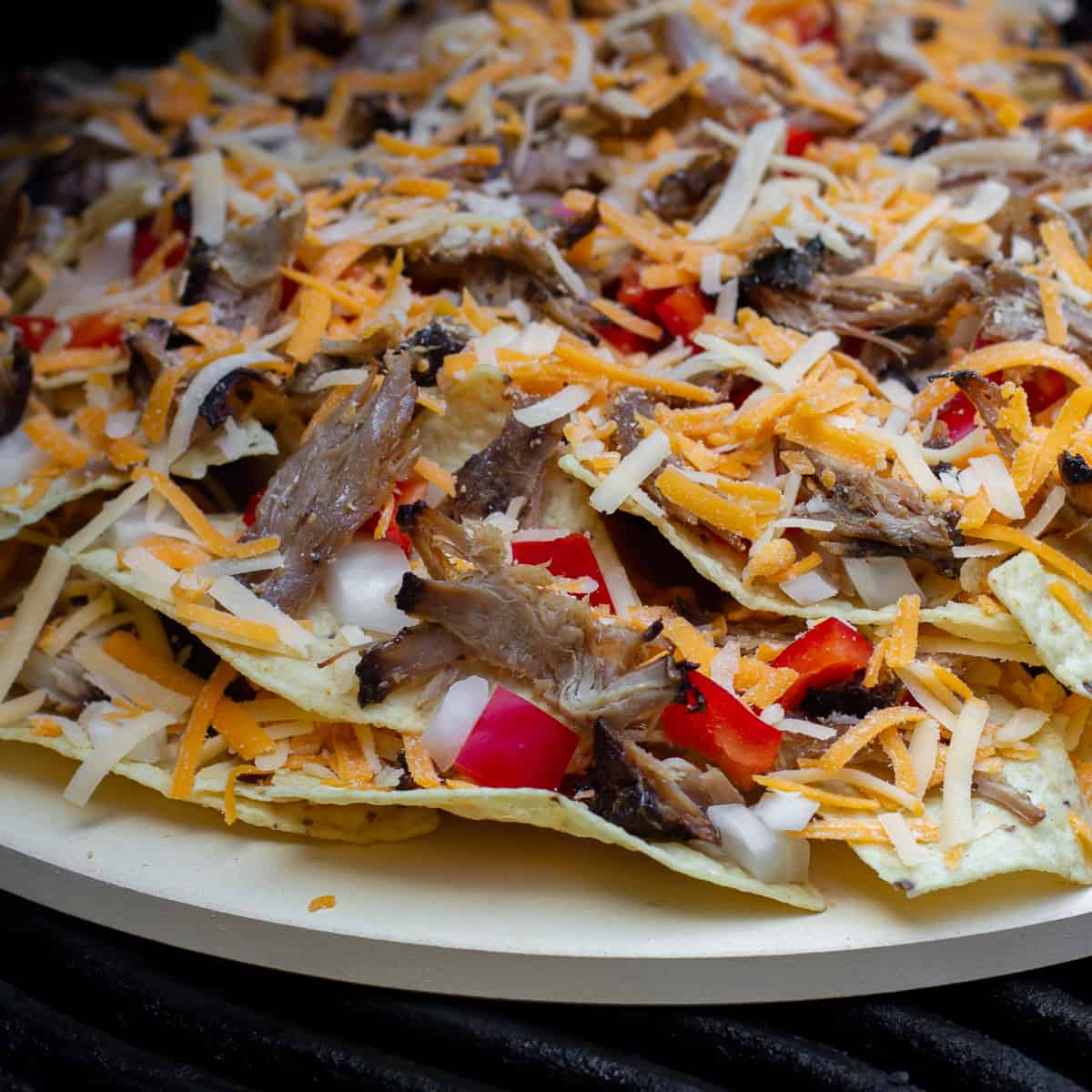 A pizza stone with nachos piled on and ready to go on the grill or in the oven.