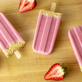 Three popsicles with halved strawberries all around them.