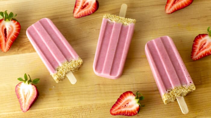 Three popsicles with halved strawberries all around them.