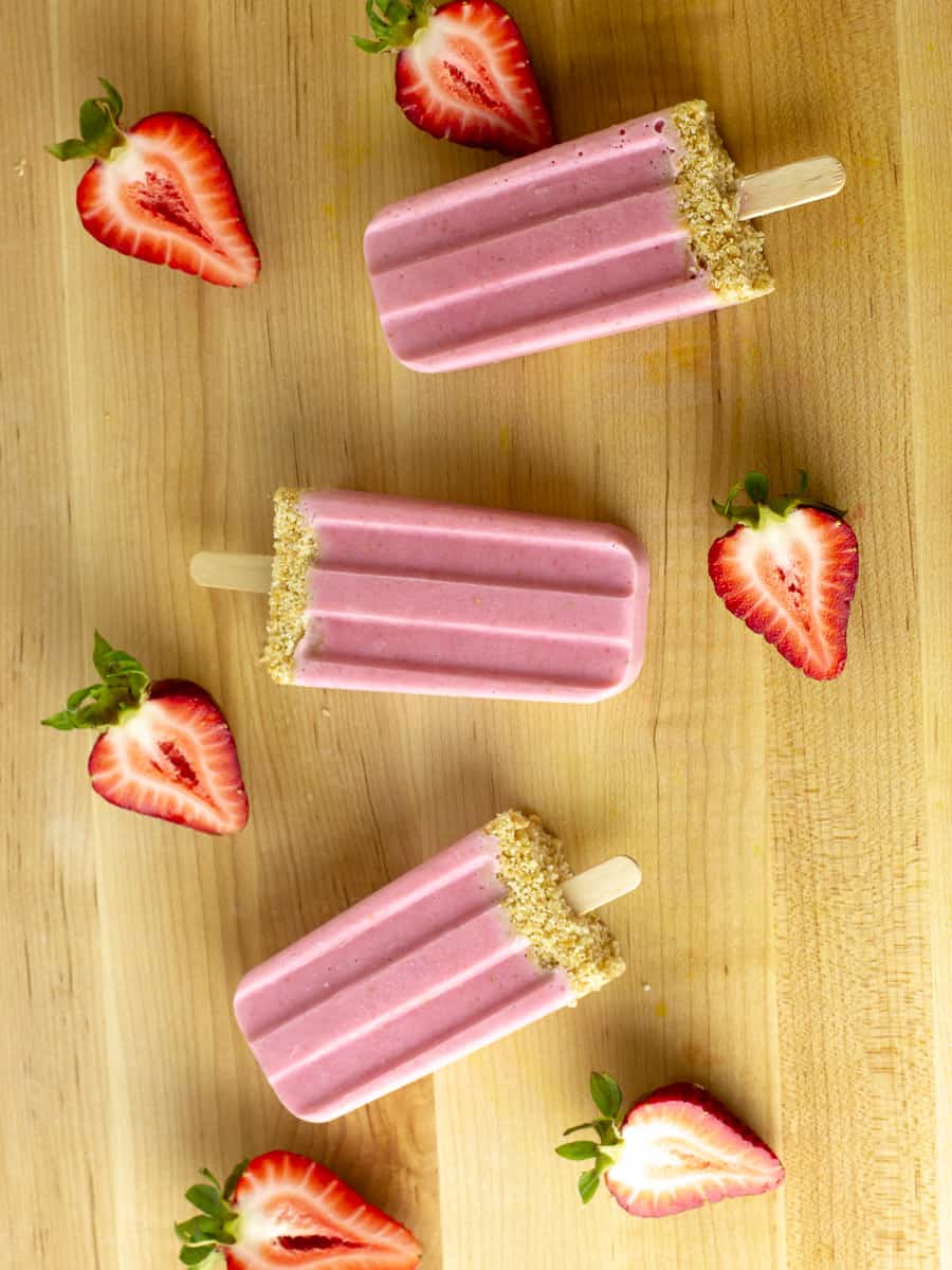 Strawberry popsicles surrounded by halved strawberries.