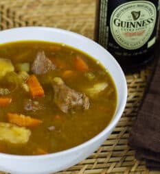 A overhead picture of a bowl of beef stew and a bottle of Guinness beer