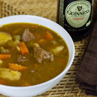 A overhead picture of a bowl of beef stew and a bottle of Guinness beer