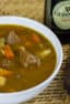 A overhead picture of a bowl of beef stew and a bottle of Guinness beer