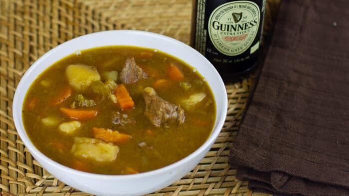 A overhead picture of a bowl of beef stew and a bottle of Guinness beer