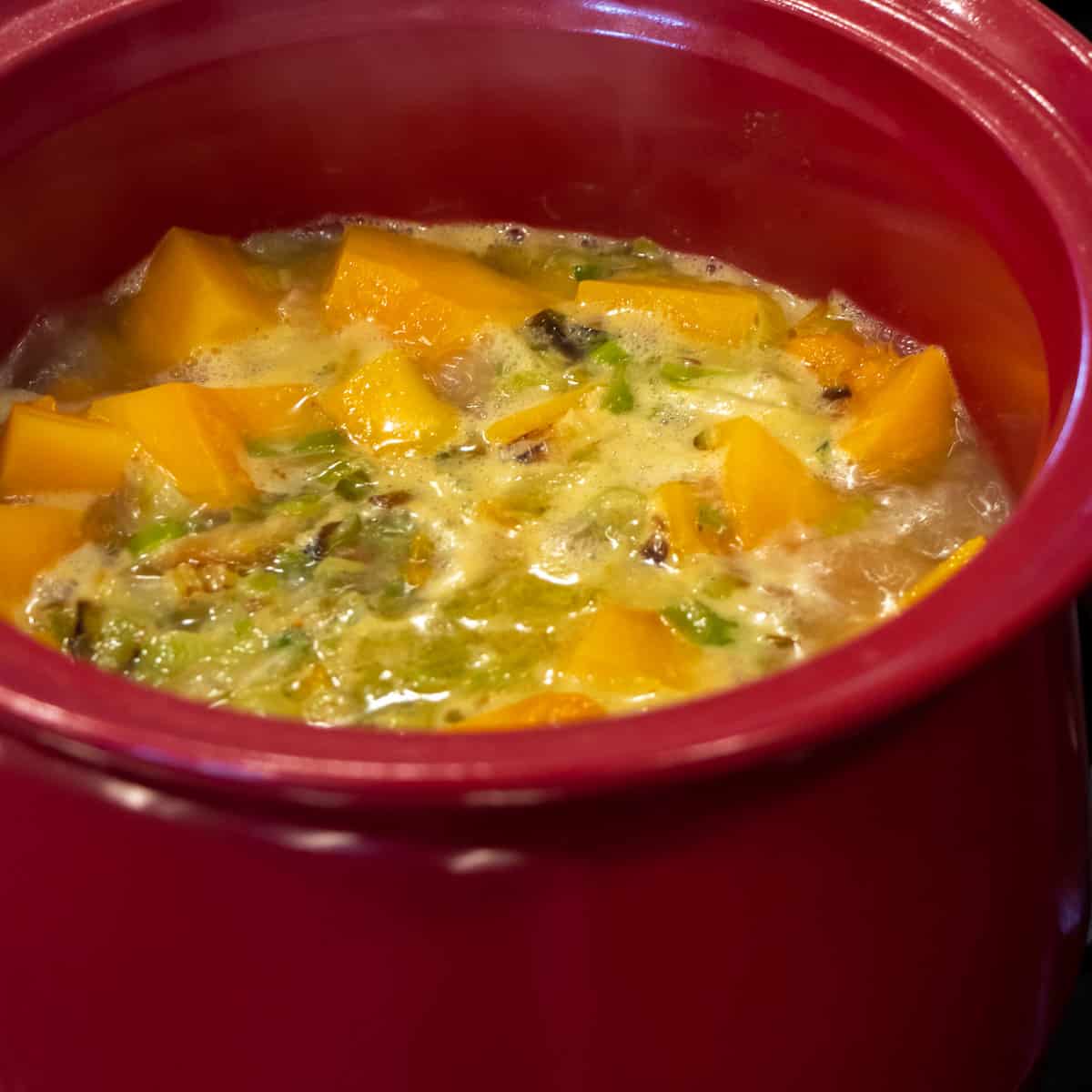 A pot with squash, leeks and onions simmering in a broth.