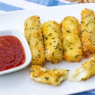 A plate of deep fried mozzarella sticks and a bowl of marinara sauce