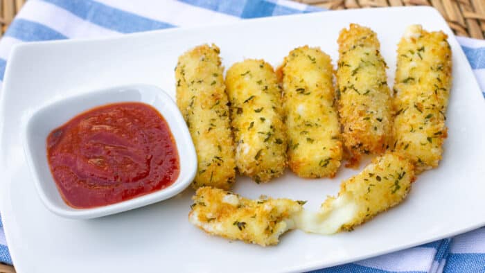 A plate of deep fried mozzarella sticks and a bowl of marinara sauce