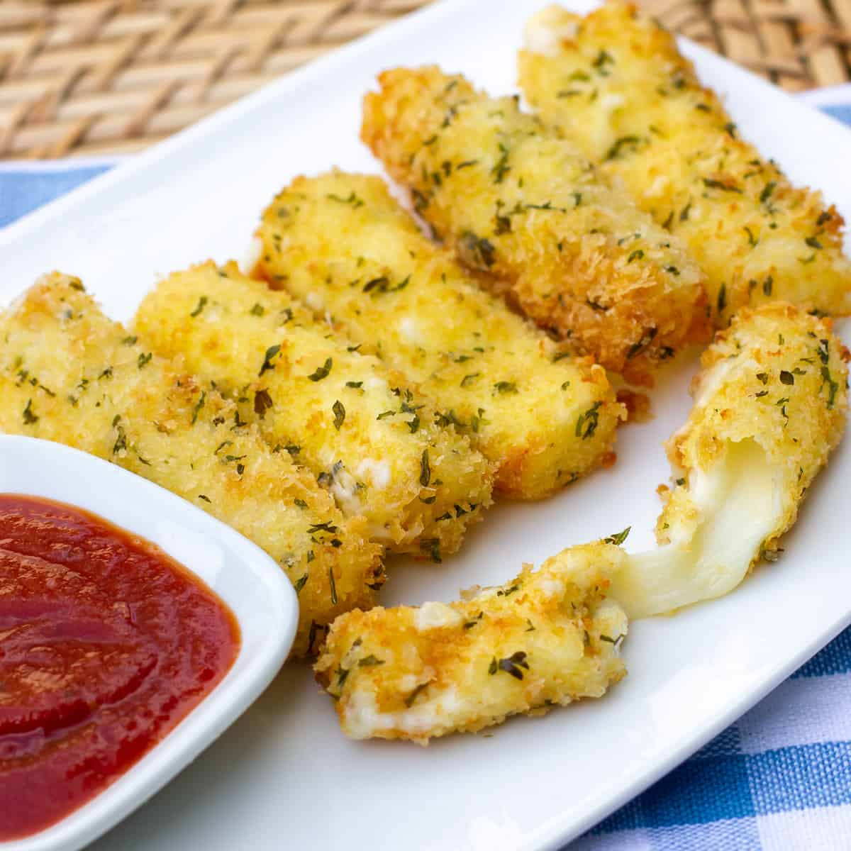 A plate of deep fried mozzarella sticks and a bowl of marinara sauce