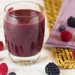 A glass of juice surrounded by berries.