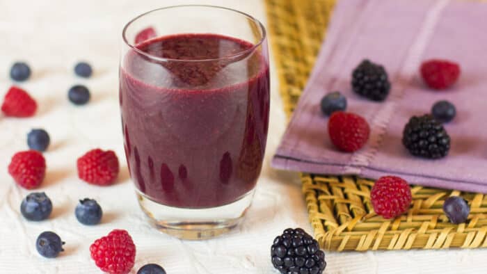 A glass of juice surrounded by berries.