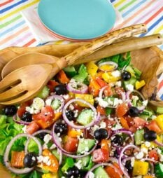 An overhead image of a large wooden bowl filled with Greek salad.