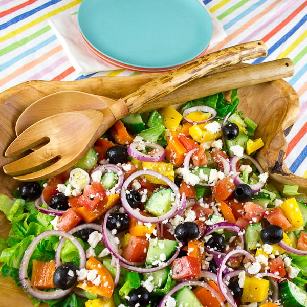 An overhead image of a large wooden bowl filled with Greek salad.