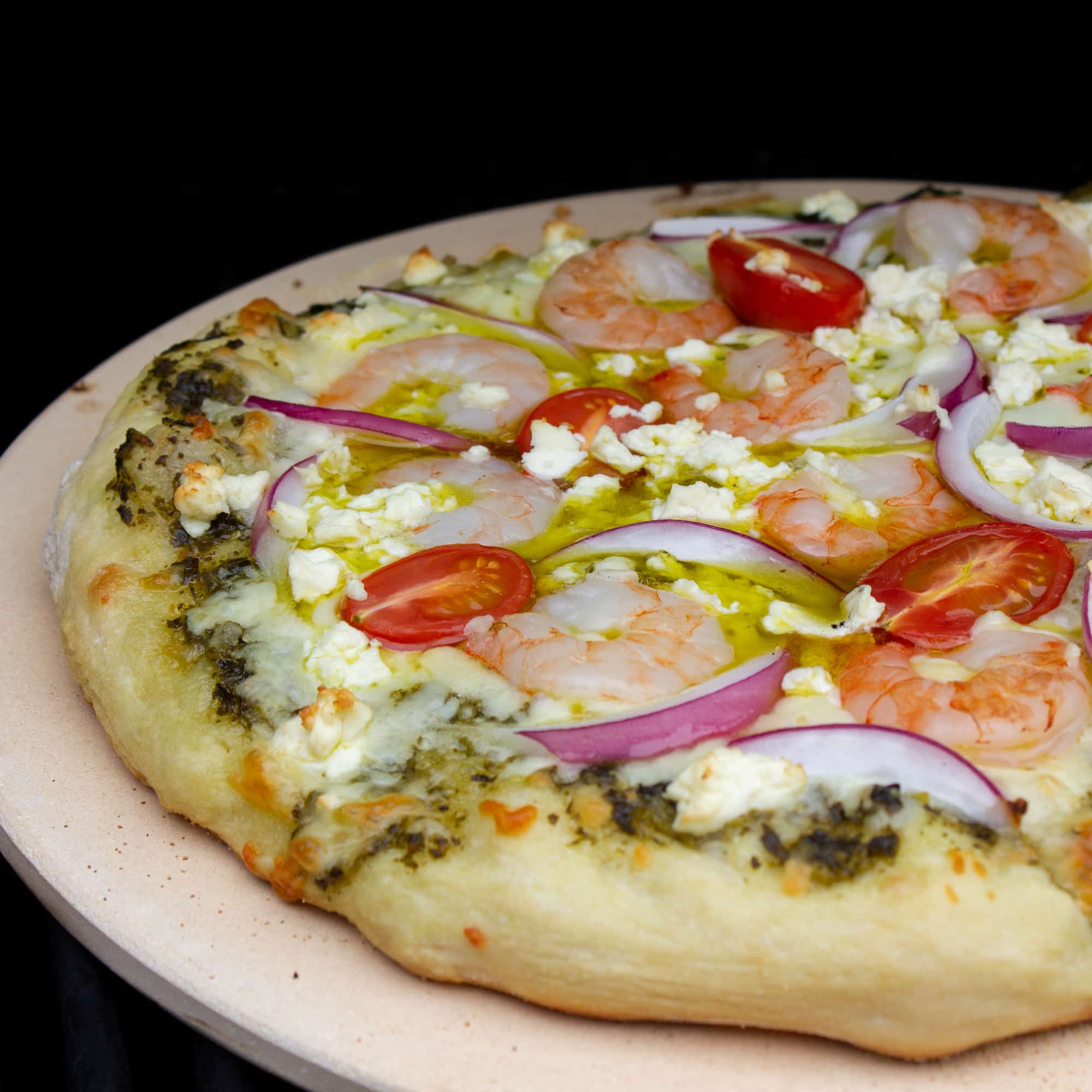 How to cook a pizza on a grill with this great BBQ pizza recipe, made with shrimp, pesto, red onions, grape tomatoes, feta cheese and mozzarella.