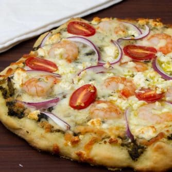 How to cook a pizza on a grill with this great BBQ pizza recipe, made with shrimp, pesto, red onions, grape tomatoes, feta cheese and mozzarella.