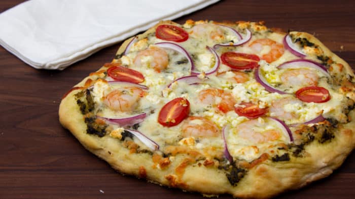 How to cook a pizza on a grill with this great BBQ pizza recipe, made with shrimp, pesto, red onions, grape tomatoes, feta cheese and mozzarella.