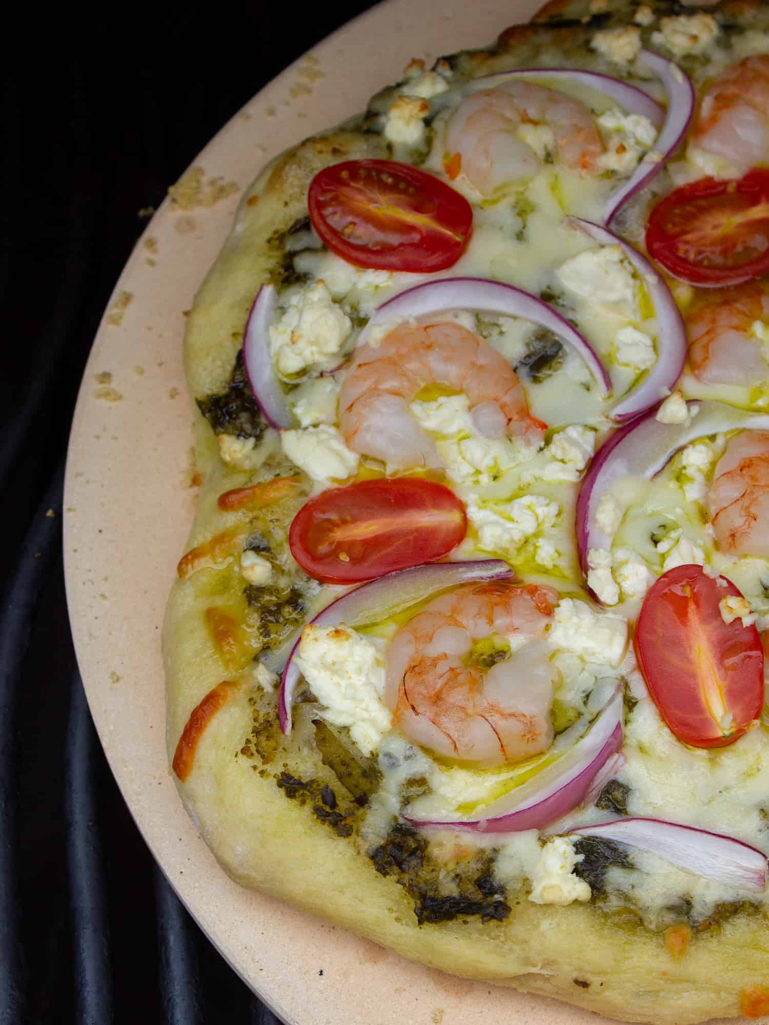 How to cook a pizza on a grill with this great BBQ pizza recipe, made with shrimp, pesto, red onions, grape tomatoes, feta cheese and mozzarella.