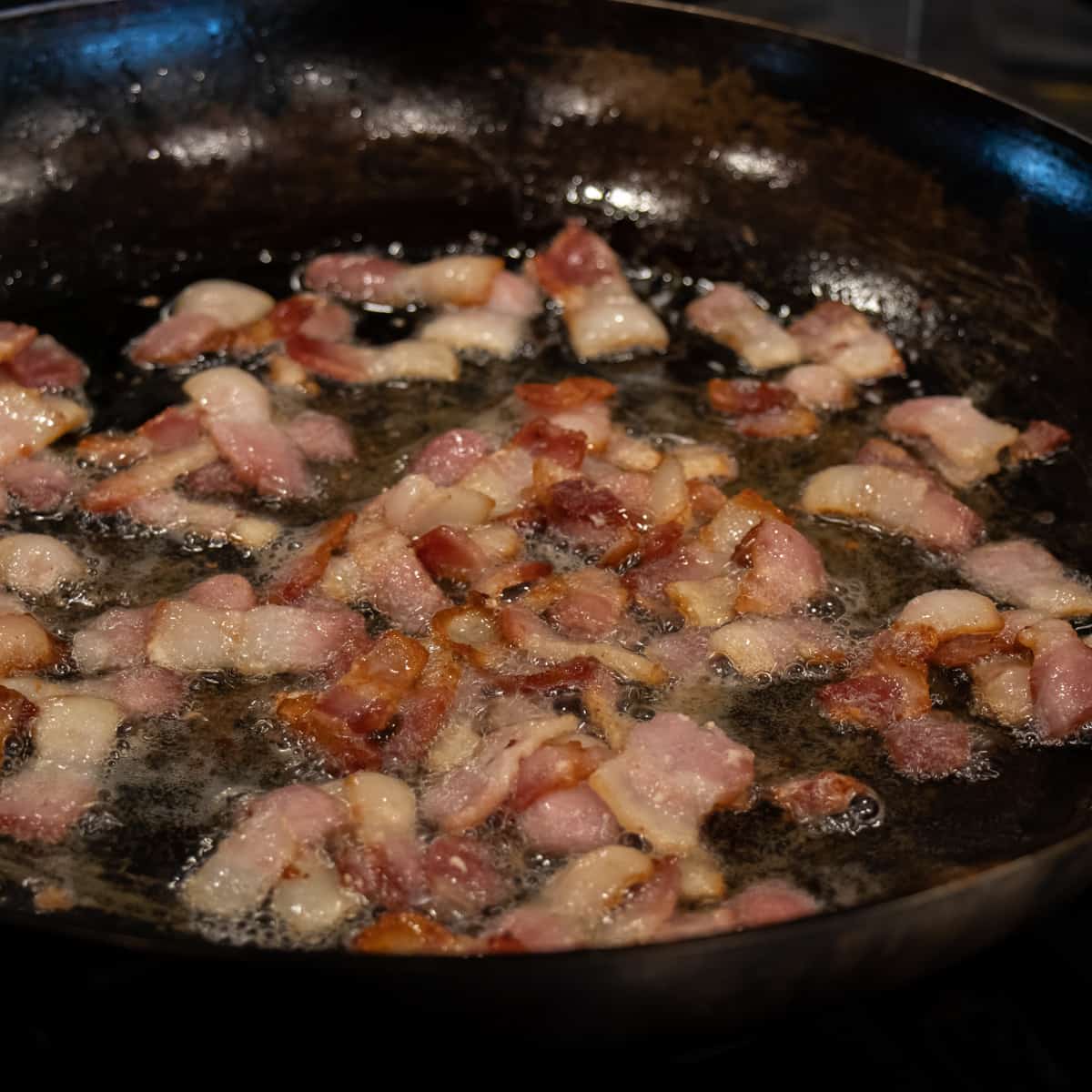 Chopped pieces of bacon frying in a skillet.