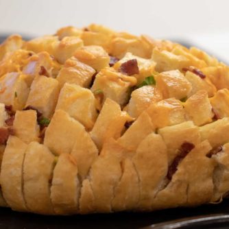 Cheesy pull apart bread made with an artisan rustic round bread loaf, sliced and filled with grated cheddar cheese, crumbled bacon and sliced green onions. Baked until cheese is bubbly!