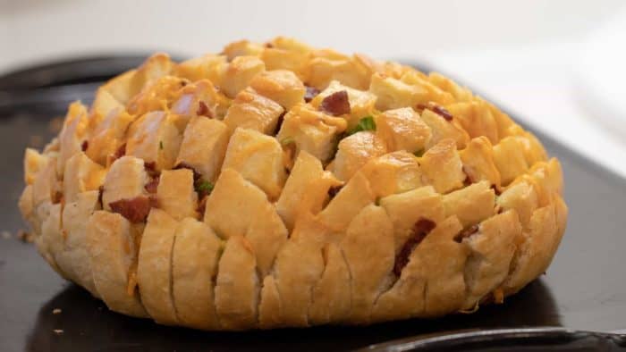 Cheesy pull apart bread made with an artisan rustic round bread loaf, sliced and filled with grated cheddar cheese, crumbled bacon and sliced green onions. Baked until cheese is bubbly!