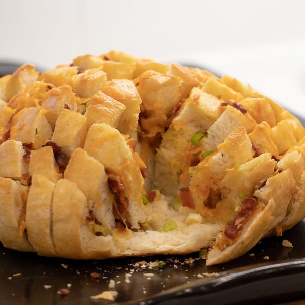 Cheesy pull apart bread made with an artisan rustic round bread loaf, sliced and filled with grated cheddar cheese, crumbled bacon and sliced green onions. Baked until cheese is bubbly!